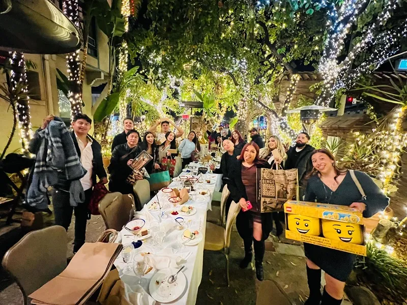 Dental Staff group lively outdoor gathering: people holding signs (including emoji face), laughing, table set for dinner under lights
